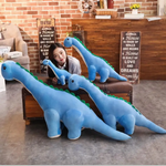 Woman with three blue Brachiosaurus plush toys of different sizes, leaning on a wooden chest.