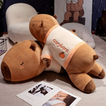 Two lying capybara plush pillows in cream shirts on a floor beside magazines