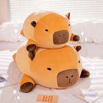 Two chubby capybara plush pillows stacked on a white bed