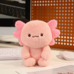 Fluffy pink axolotl plush sitting on a desk beside a keyboard and mouse