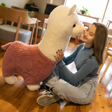 Woman sitting on the floor hugging a large alpaca plush with a pink body