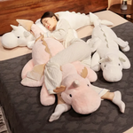 Woman cuddling a pink dragon plush body pillow on a bed, surrounded by white dragon pillows.