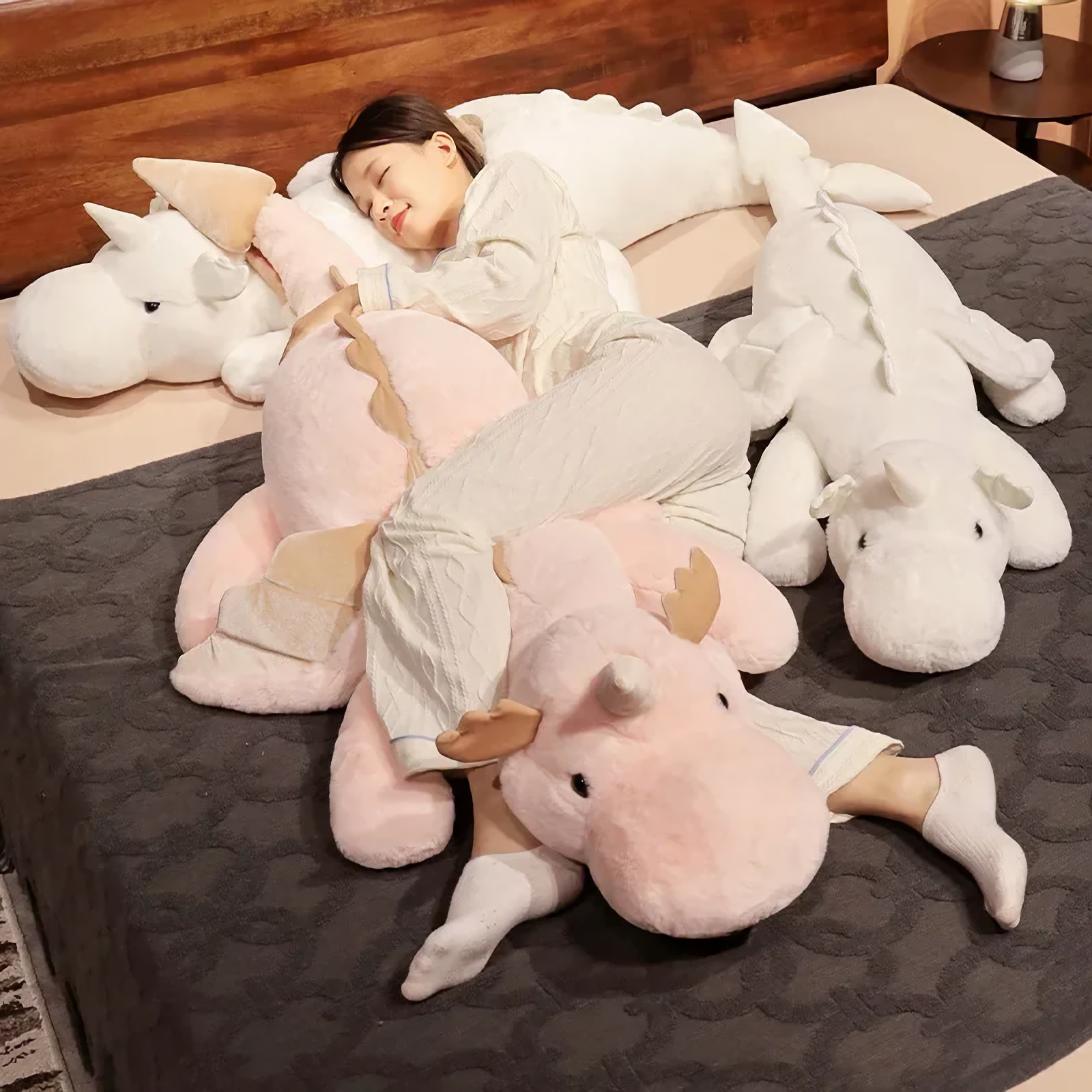 Woman cuddling a pink dragon plush body pillow on a bed, surrounded by white dragon pillows.