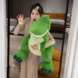 Woman holding a big green T-Rex plush with a toothy smile and dark teal claws, standing in front of a mesh screen.