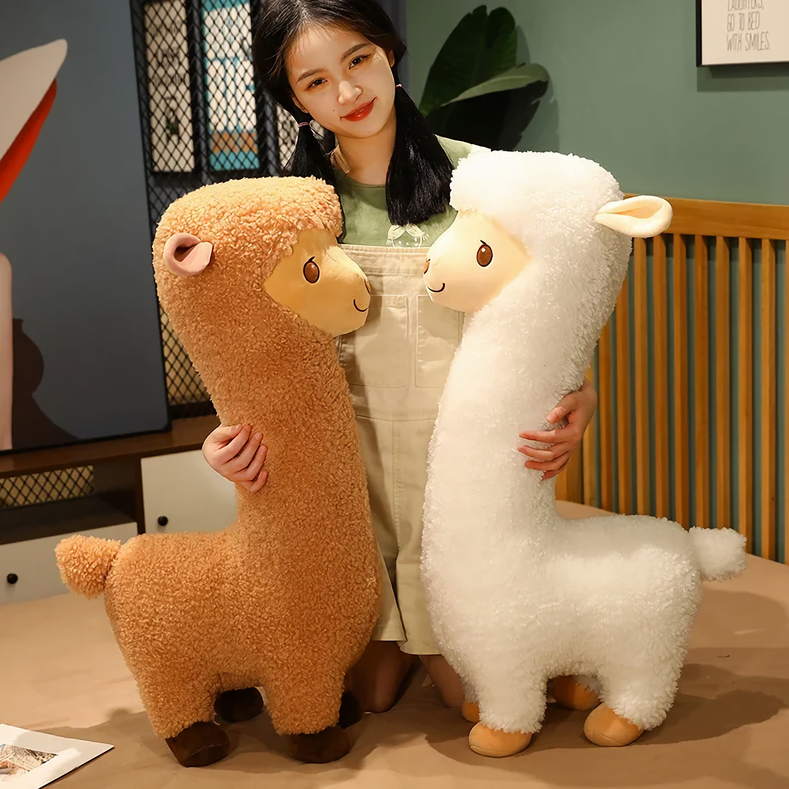 Woman smiling behind a white alpaca plush and a brown alpaca plush