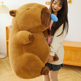 Woman standing beside a large brown capybara plush with a blue nose bubble