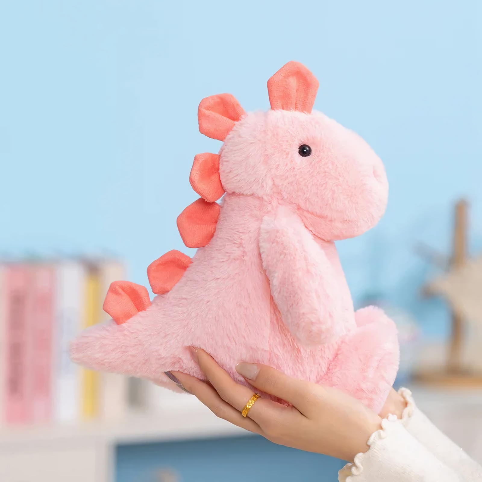 Hand holding a pink dinosaur plush with coral spikes against a blue background