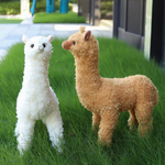 White and brown standing alpaca plushies side by side on a green lawn