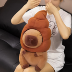 Person sitting on a sofa holding a capybara plush with a brown swirl hat