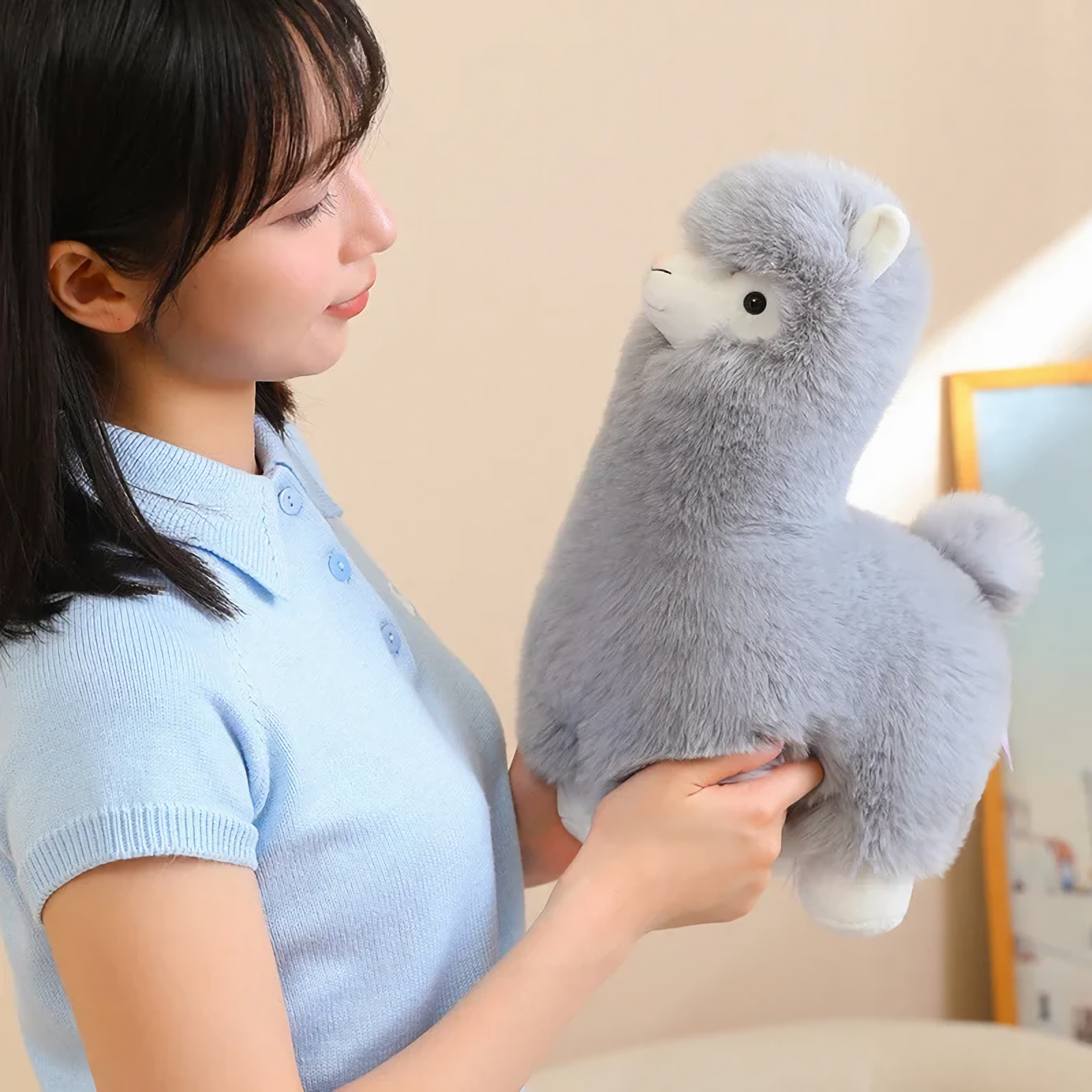 Woman holding a gray alpaca plush and looking at it