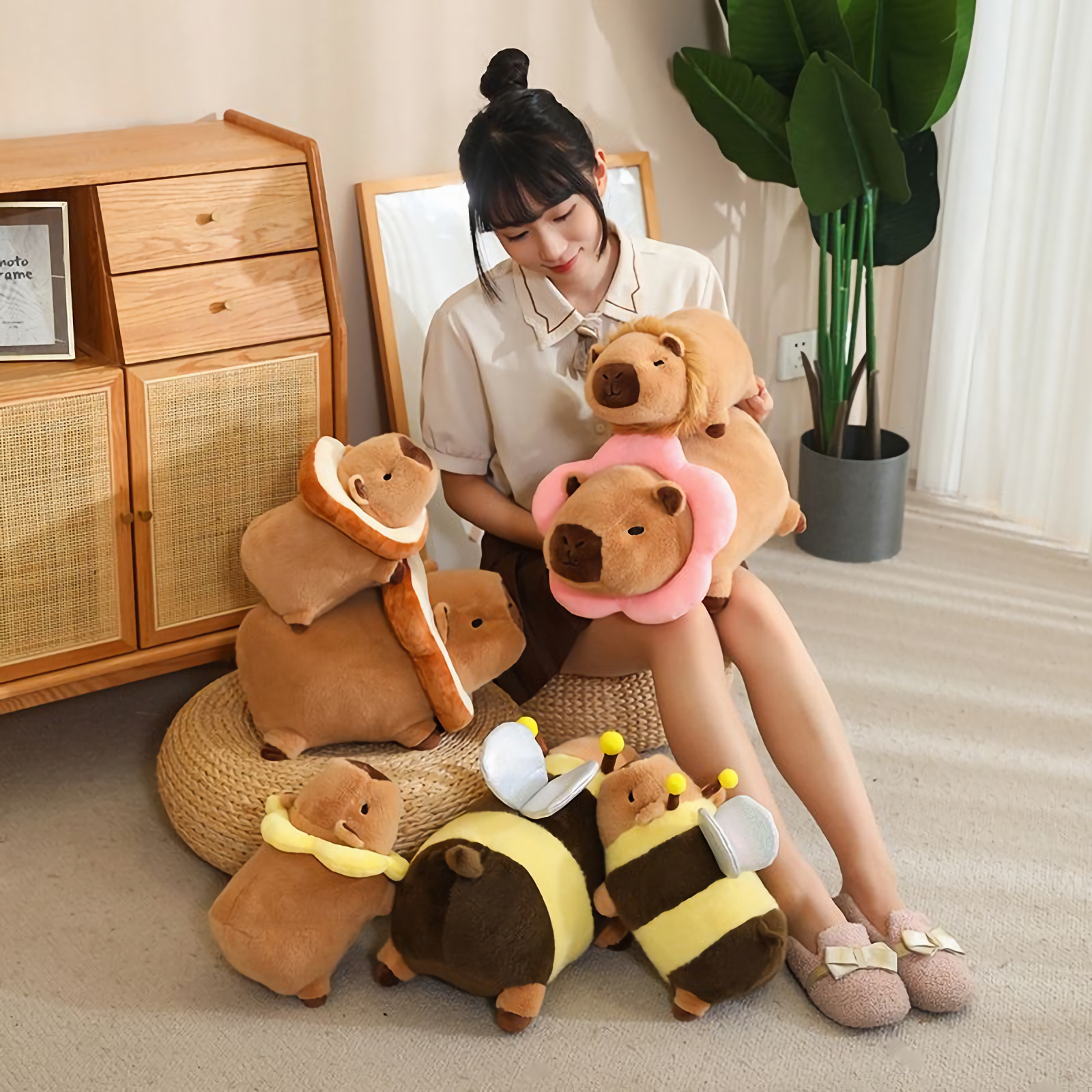 Woman sitting on the floor with capybara plushies in bread, flower and bee costumes