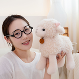 Woman with round glasses holding a white curly lamb plush with pink ears