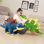 Woman sitting on a floor with a blue Stegosaurus plush and a green Stegosaurus plush