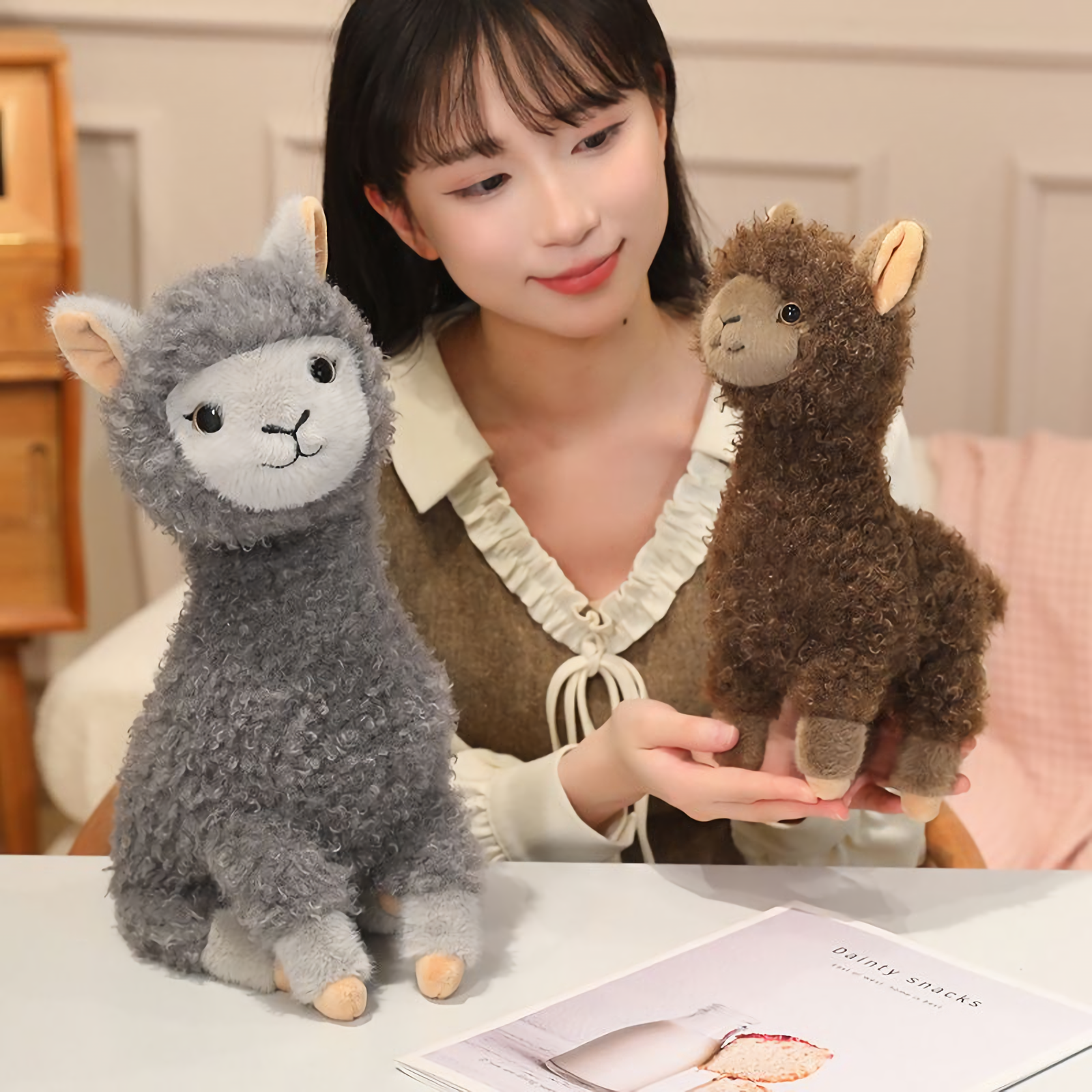 Woman smiling next to a gray alpaca plush while holding a small brown one