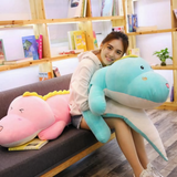 Woman leaning on a long blue dinosaur plush body pillow next to a pink one on a sofa