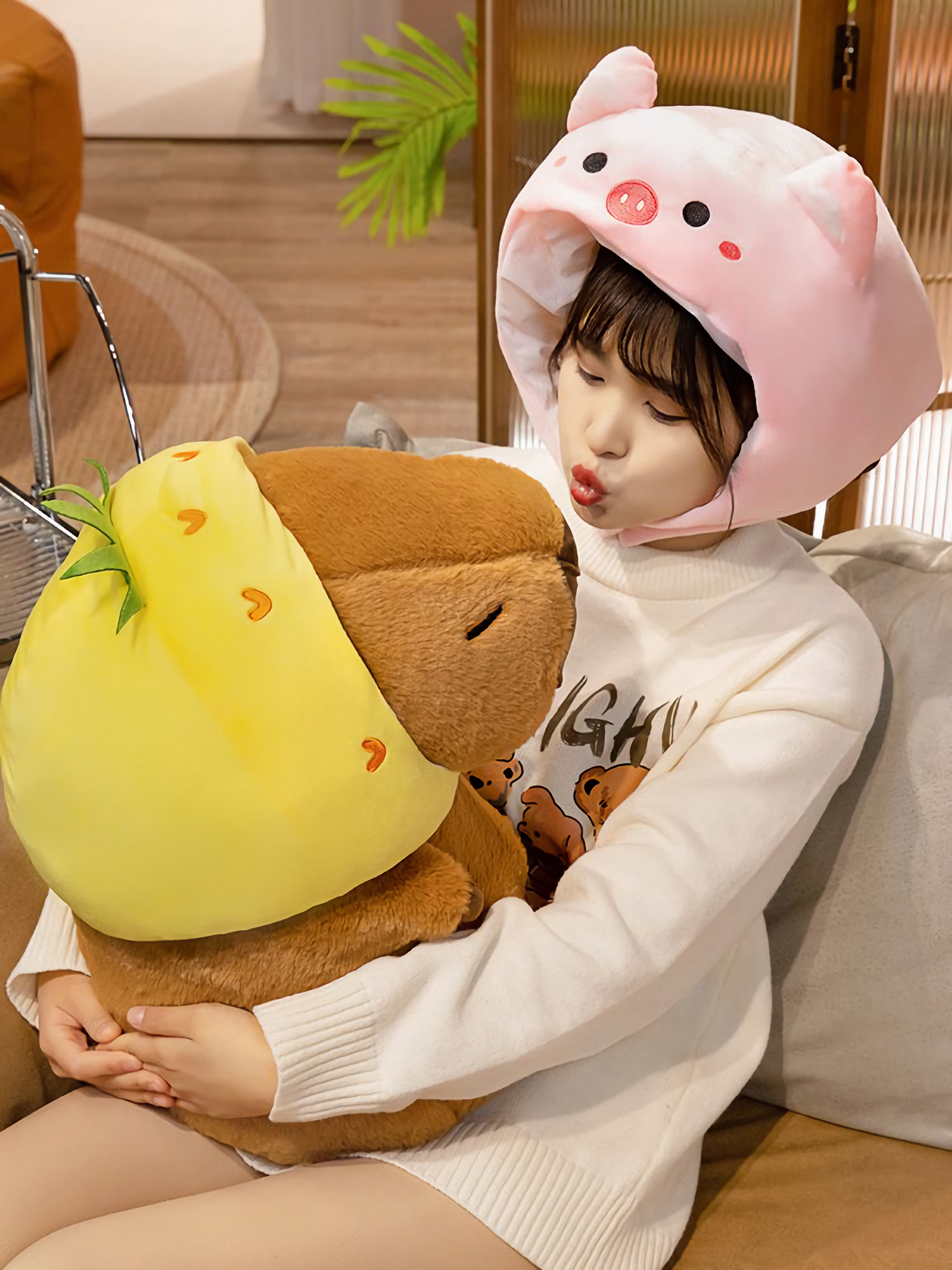 Woman in a pig hat holding a capybara plush in a pineapple hood