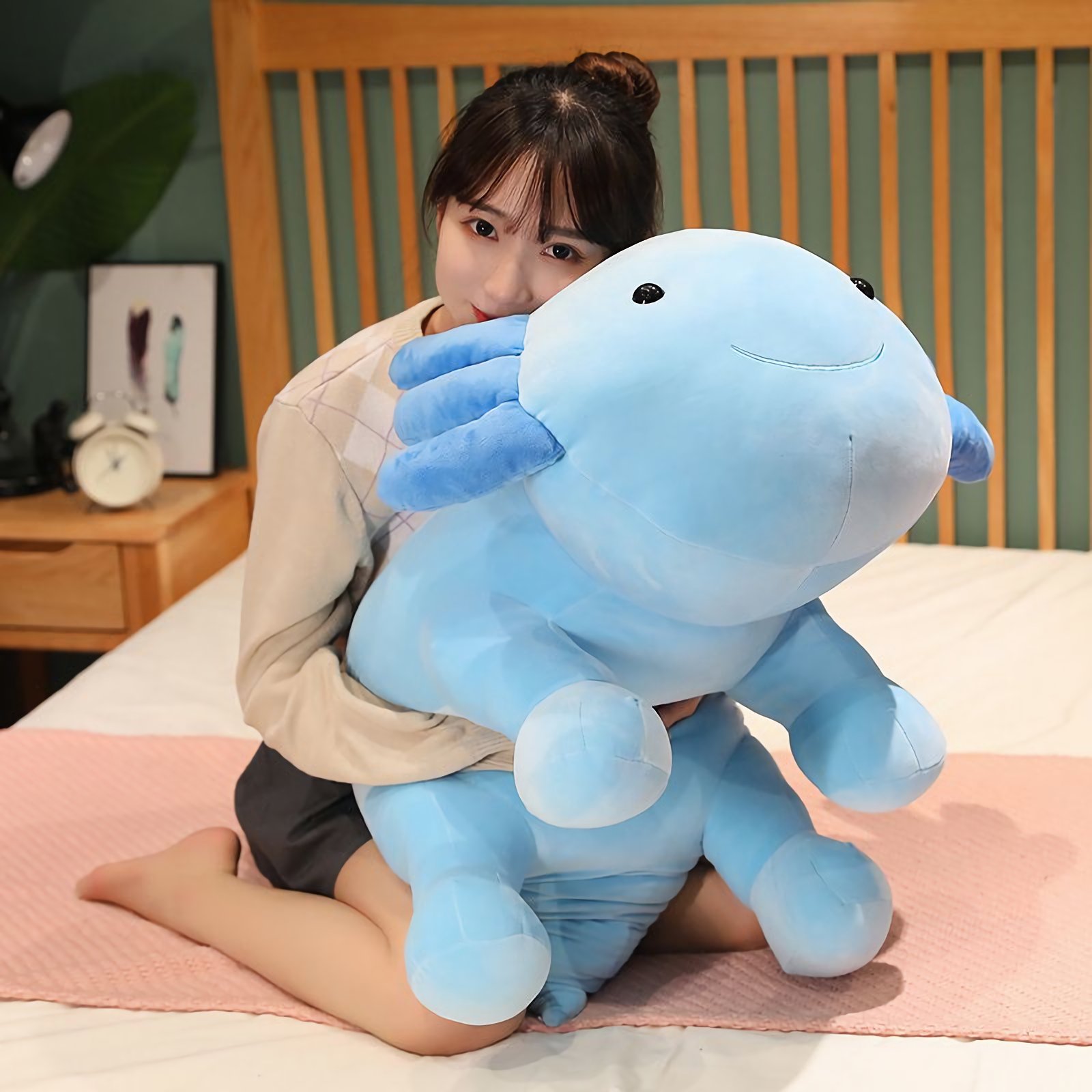 Girl hugging a large blue axolotl plush on a bed with a wooden headboard