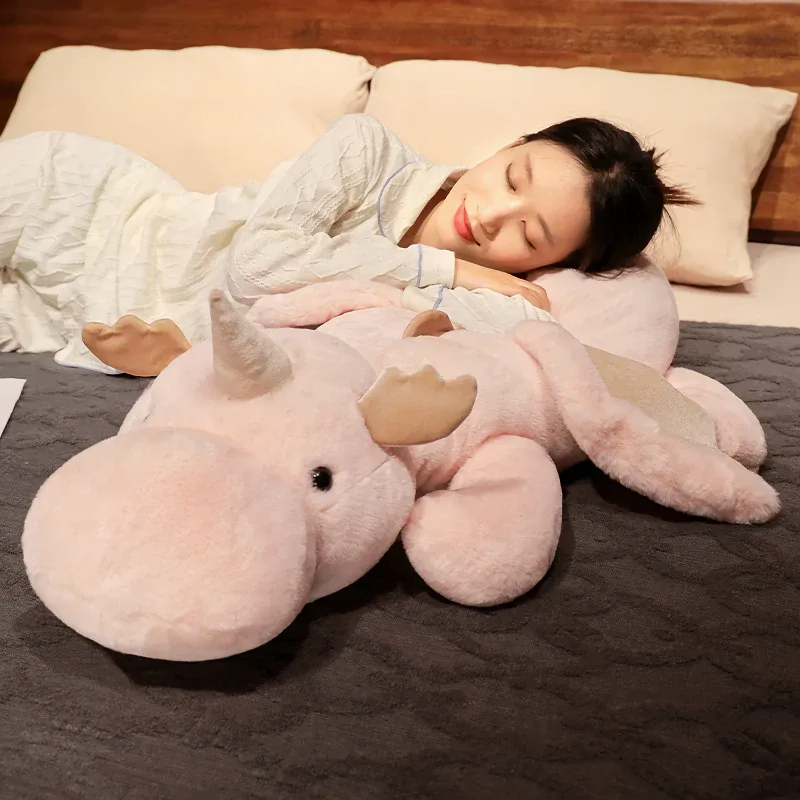 Woman sleeping on a bed hugging a pink and white dragon plush body pillow.