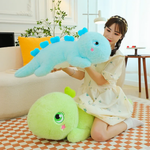 A woman holds a blue giant dinosaur plush pillow, with a green one on the floor nearby.