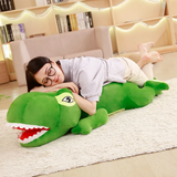 Woman with glasses resting on a long green T-Rex plush pillow on a white rug