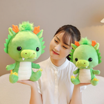 Woman holding two green dragon plush toys with orange horns, one in each hand.