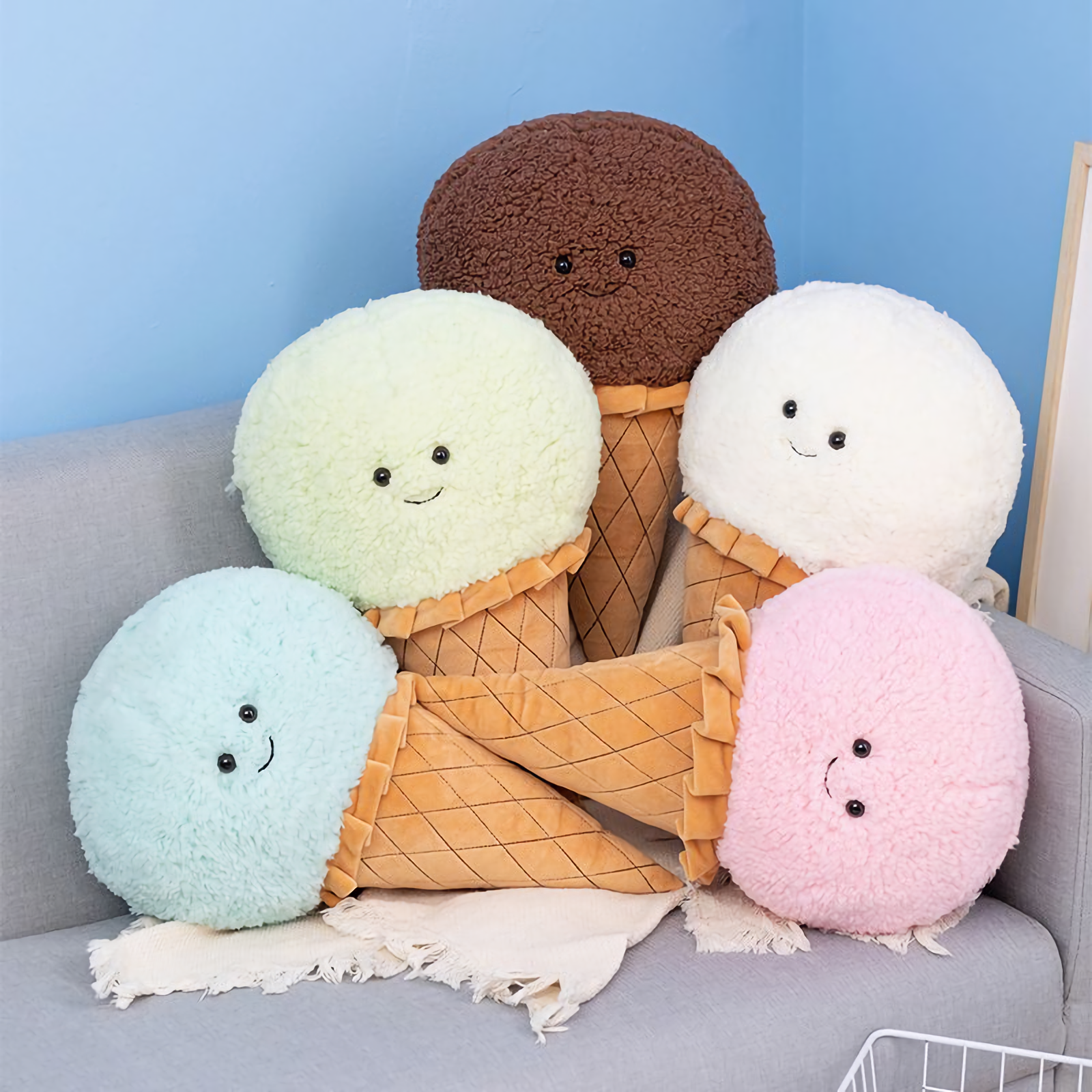 Five ice cream cone plush pillows in pink, blue, mint green, white and brown on a gray sofa