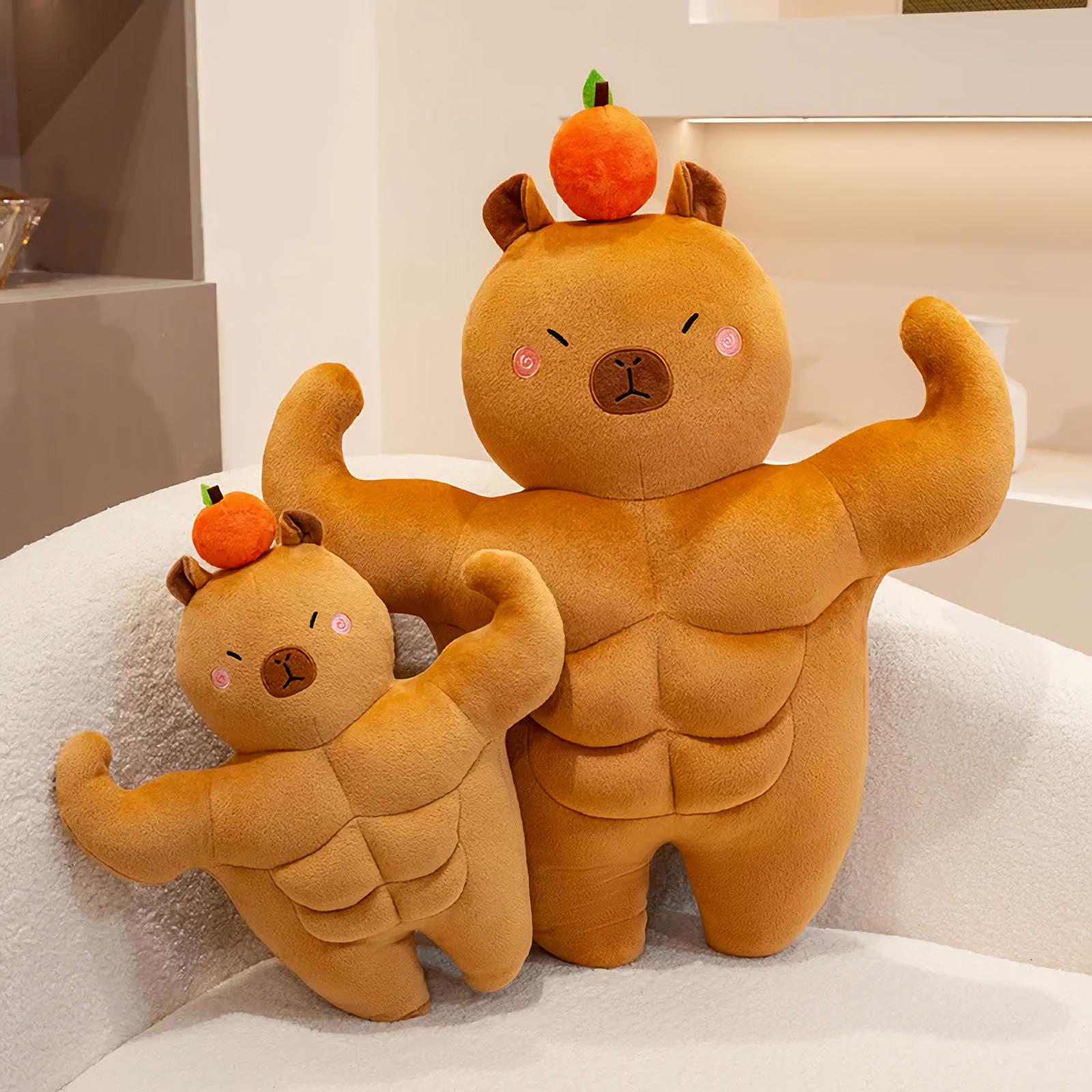 Two muscle capybara plushies in different sizes on a white sofa
