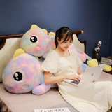 Woman working on a laptop on a bed with two rainbow dinosaur plush pillows