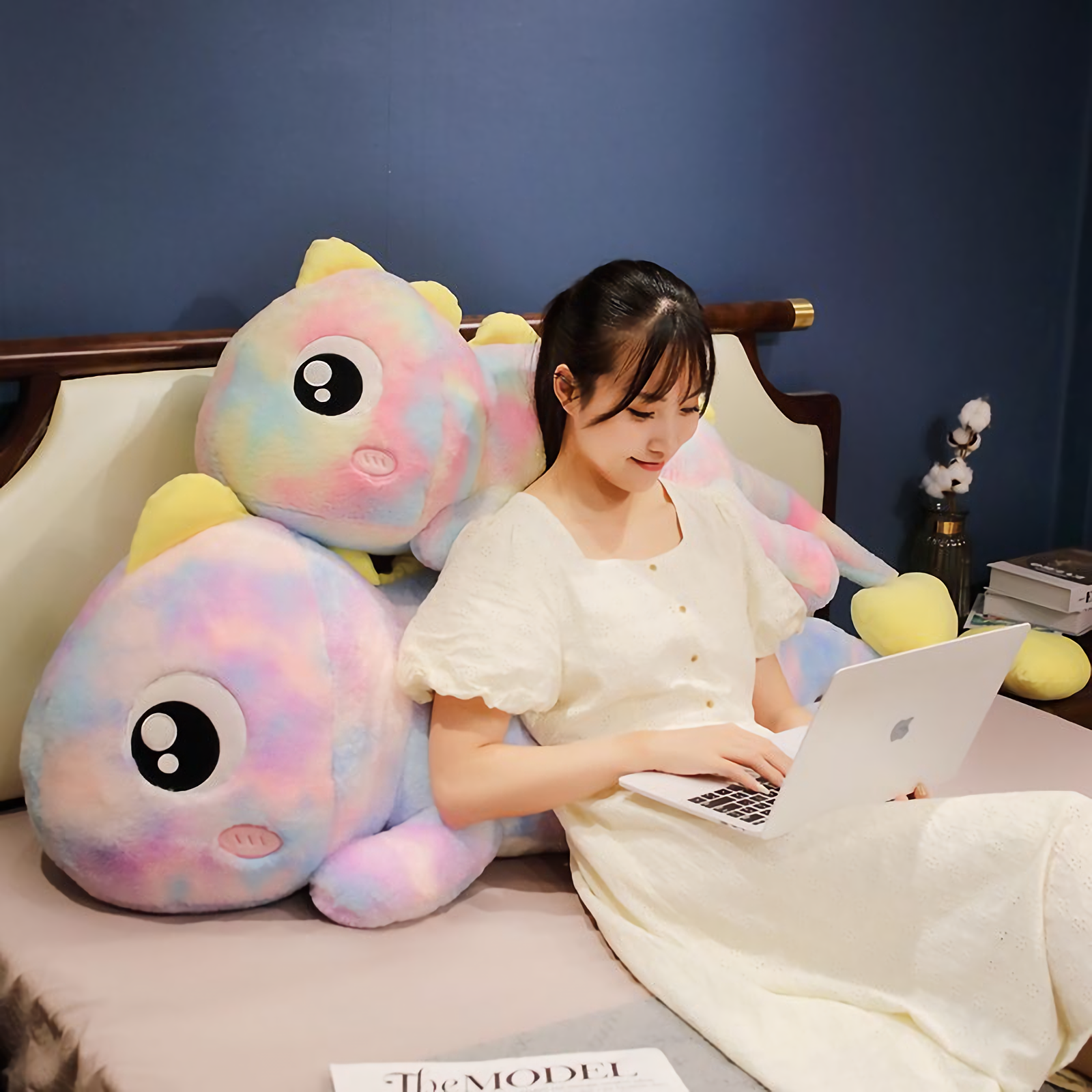 Woman working on a laptop on a bed with two rainbow dinosaur plush pillows