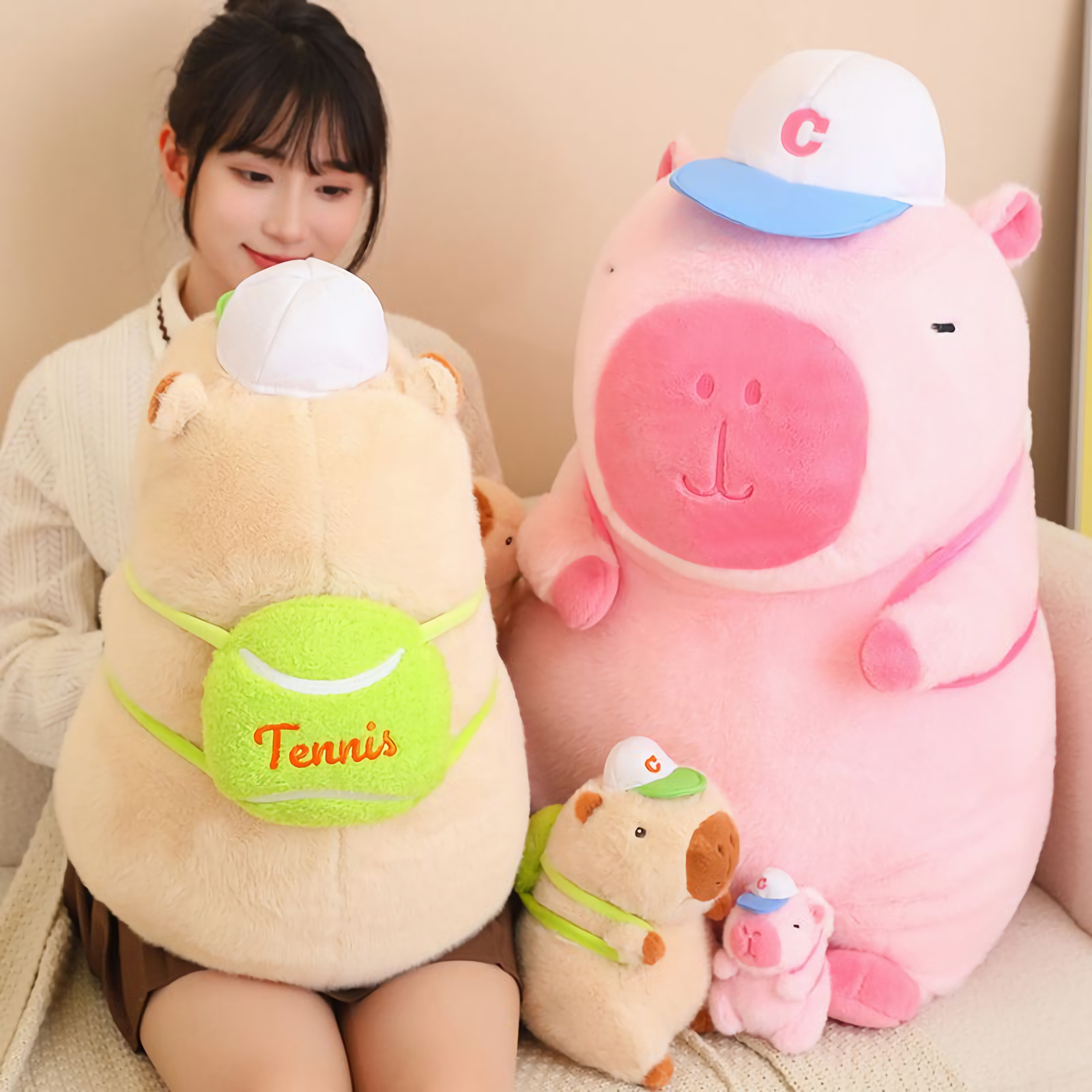 Woman holding a large brown capybara plush with a tennis ball bag beside a pink one