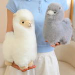 Woman holding a white alpaca plush beside a gray alpaca plush