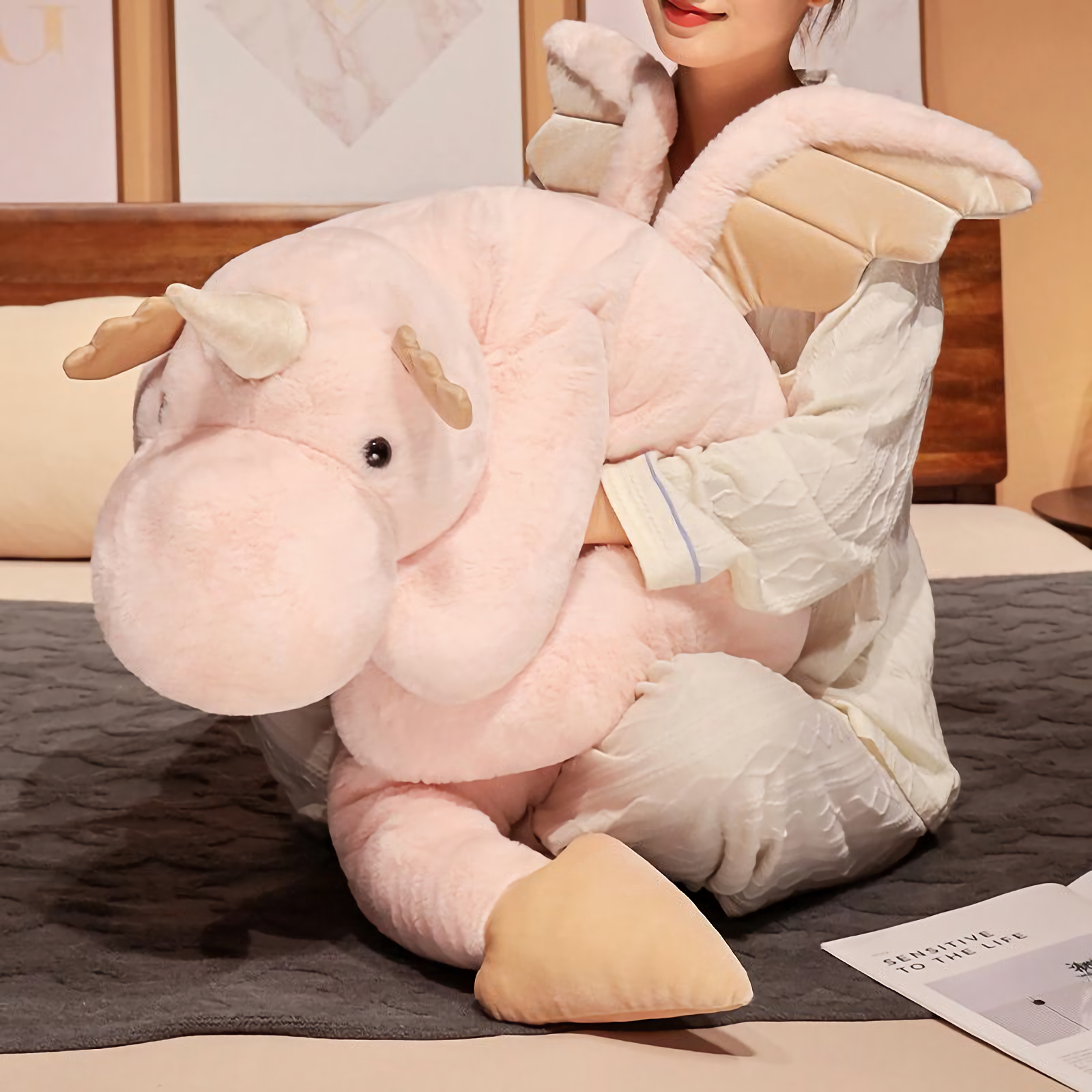 Woman hugging a large pink dragon plush with a small horn and soft wings