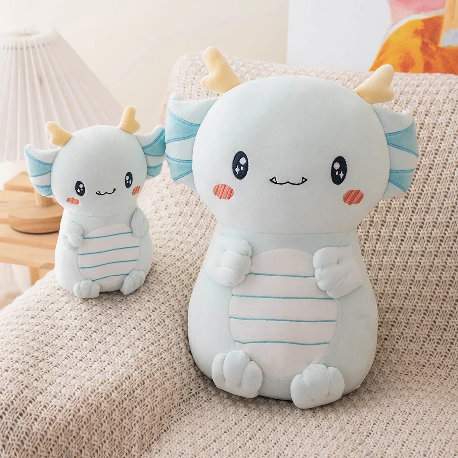 Small and large light blue axolotl dragon plushies sitting on a cream sofa