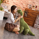 Woman sitting on the floor hugging a green Brachiosaurus dinosaur plush with cream belly and back spikes.
