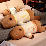 Three lying capybara plush pillows in cream shirts with yellow and orange trim on a bed