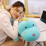 Woman resting her head on a blue dinosaur plush pillow beside an open laptop