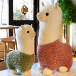 Green body alpaca plush and a large pink body alpaca plush on a table