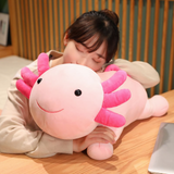 Girl resting her head on a big pink axolotl plush pillow with a smiling face