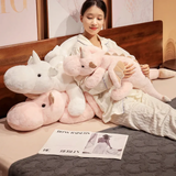 Woman hugging pink and white dragon plush body pillows on a bed, wearing cozy pajamas, with an open magazine nearby.