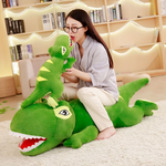 Woman sitting beside a long green T-Rex plush pillow with a smaller green plush on top