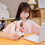 Woman at a desk with a laptop and a white graduation capybara plush