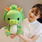 Woman holding cute green dragon plush with orange horns, cream belly, and lime snout.
