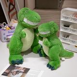 Two smiling green T-Rex dinosaur plush toys on a table, showing size difference; one larger, one smaller.