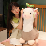 Woman smiling while hugging a gray alpaca plush with headphones on a bed