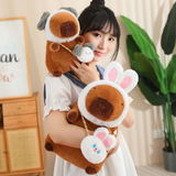 Woman hugging capybara plushies in rabbit and dog hoods with matching bags