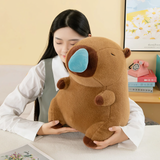 Woman hugging a brown capybara plush with a blue nose bubble at a desk