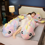 Woman lying on a bed beside two rainbow dinosaur plush body pillows