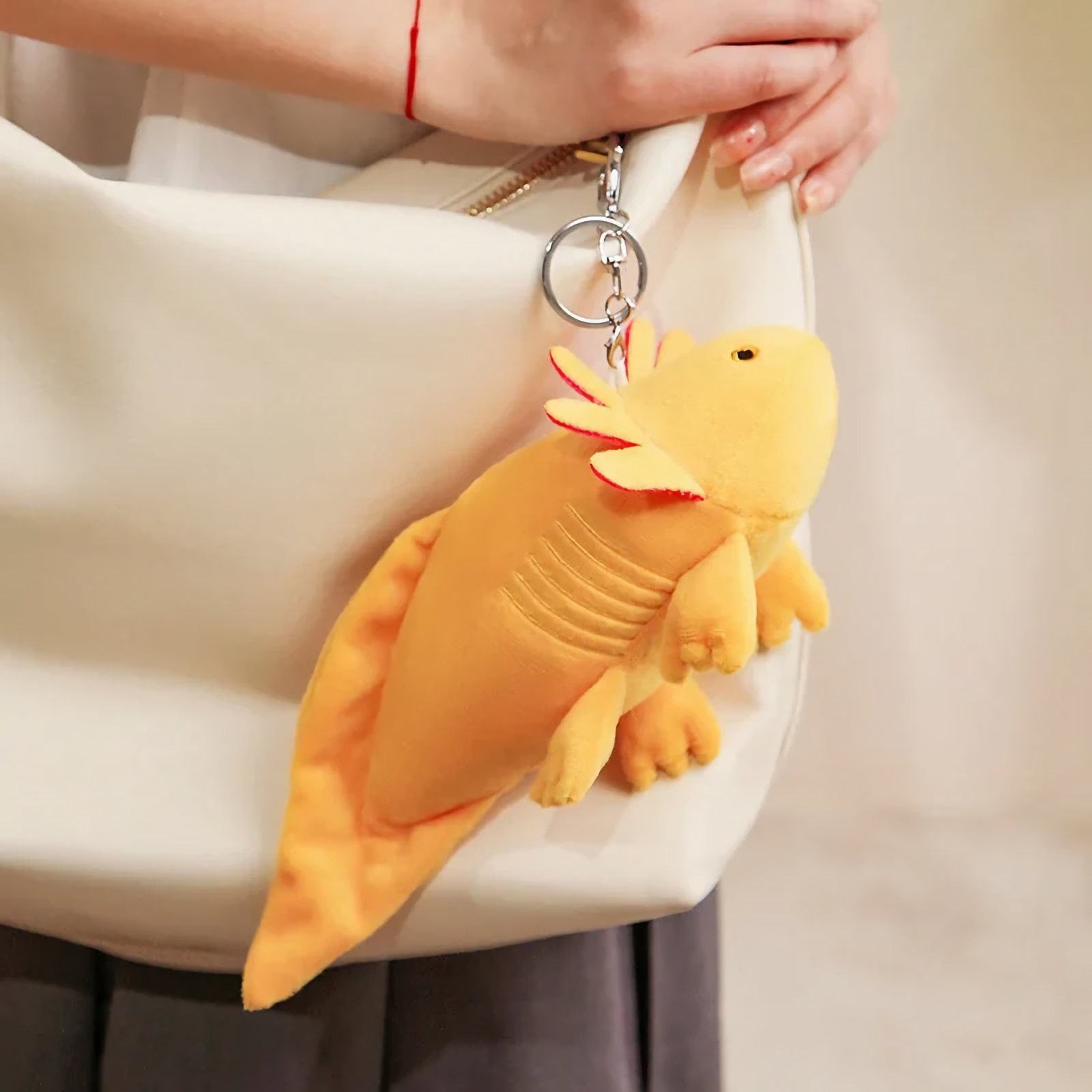 Yellow axolotl plush with a clip ring hanging from a white tote bag held by a woman