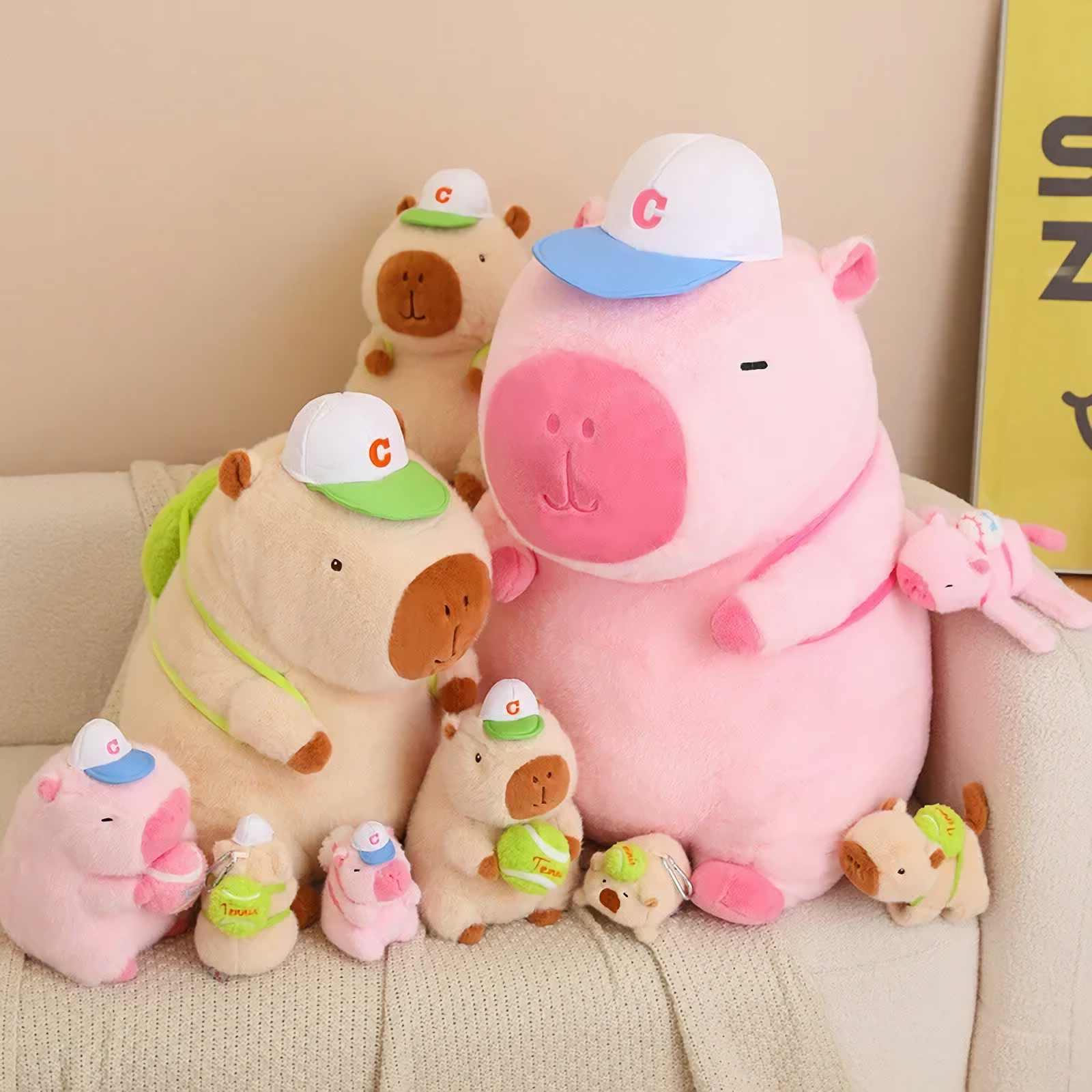 Sporty brown and pink capybara plushies in several sizes on a sofa