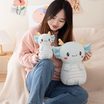 Girl on a sofa holding two light blue axolotl dragon plushies of different sizes
